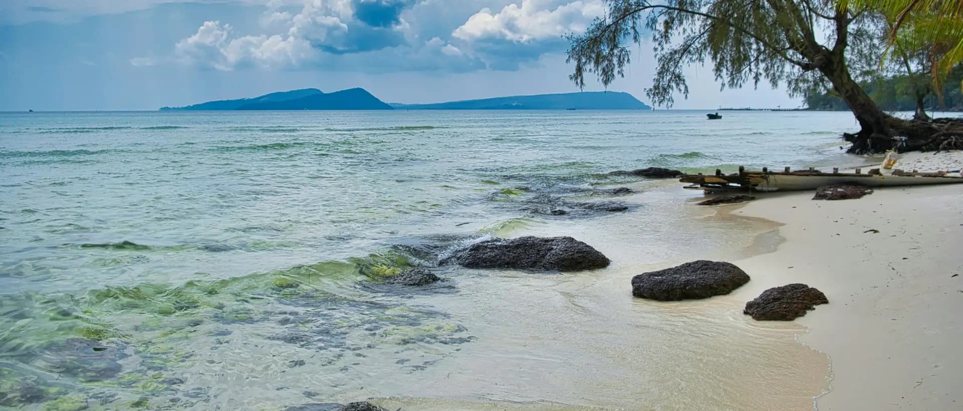 Lazy Beach on Koh Rong: white sand, dark rocks and clear water, with islands on the horizon